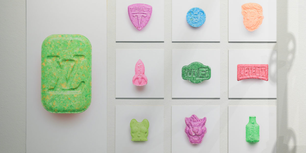 Een foto van 10 foto's aan een muur waarop steeds één xtc-pil te zien is op een witte achtergrond.