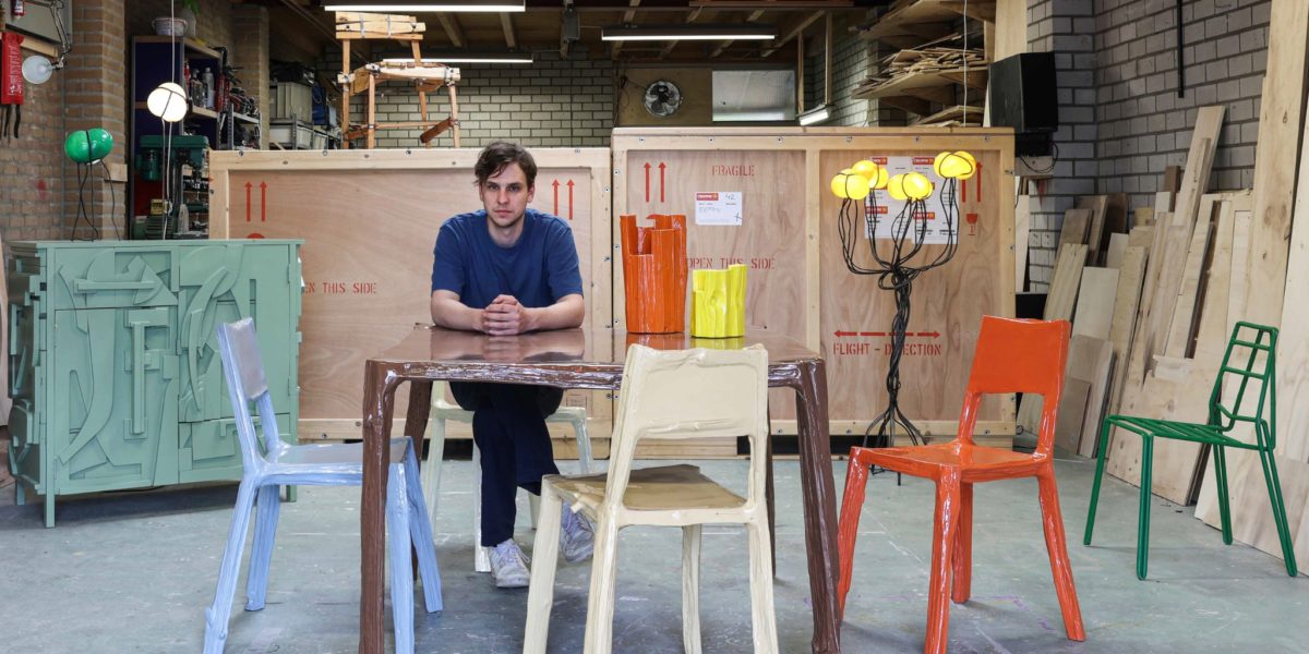 Teun zwets zittend aan een door hem ontworpen tafel in zijn studio omringd door kleurrijke meubels.