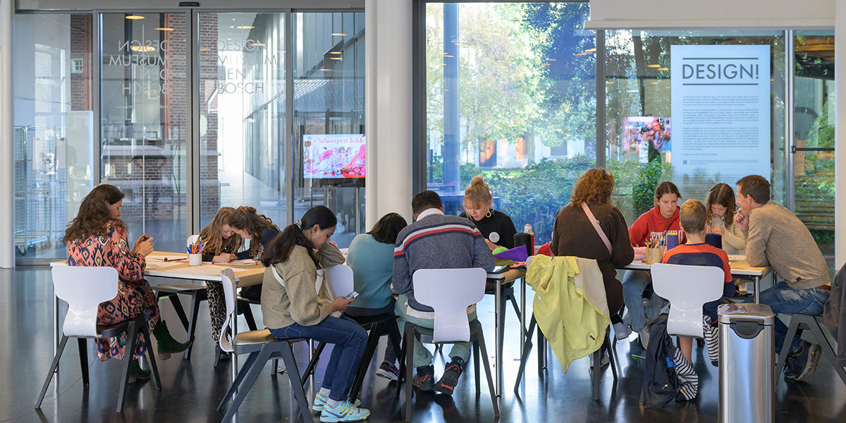 Een groep mensen zit aan een tafel in de hal van het museum te knutselen.