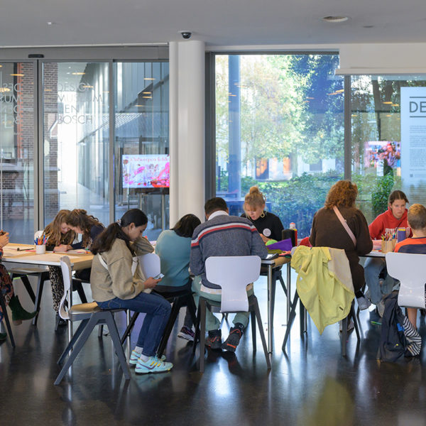 Een groep mensen zit aan een tafel in de hal van het museum te knutselen.