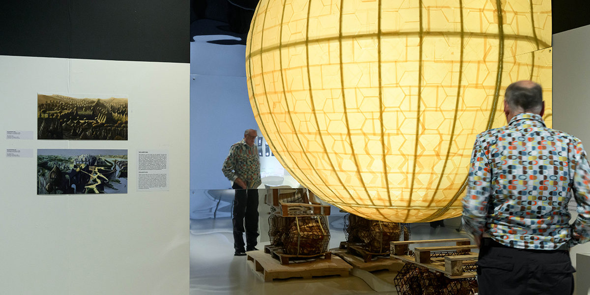 Man kijkt in tentoonstellingszaal naar een 3 meter hoge, gele wereldbol van bijenwas.