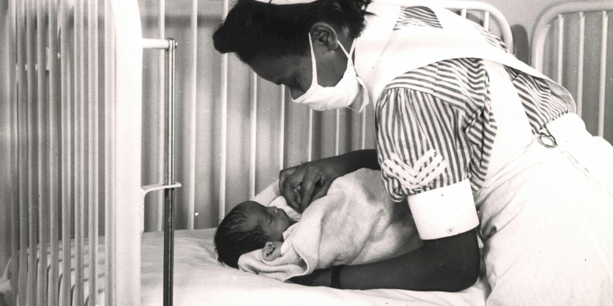 Historische foto van verpleegster die zich over een baby buigt.