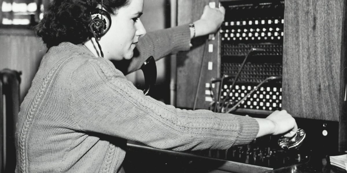 Een historische foto van een vrouw die een telefoonsysteem bediend.